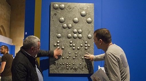 La primera de las 139 obras de la exposición, que firma el salmantino Juan Francisco Pro es la única que puede tocar y manosear el visitante. De hecho se trata de un repujado e hidrolizado en cobre y zinc en el que aparecen el relieve escritas en braille en varios idiomas el título de la exposición