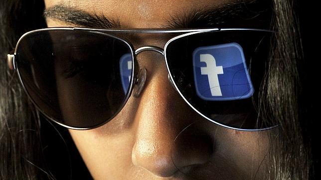 El logo de Facebook se refleja en las gafas de una joven