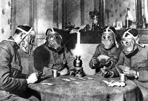 In anticipation of a chemical attack, these soldiers play cards while wearing gas masks