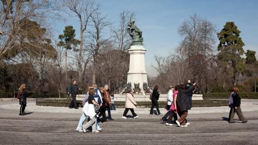 Varios paseantes pasan por delante de la estatua del Ángel Caído