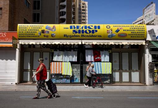 Transeúntes junto a un comercio cerrado por el estado de alarma en Benidorm