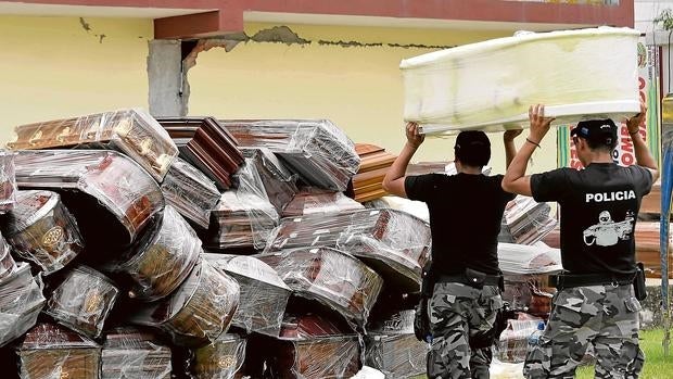 Dos policías apilan ataúdes para algunas de las 499 víctimas del seísmo, según la última cifra ofrecida por el Gobierno