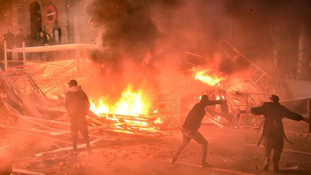 Manifestantes lanzan proyectiles frente a una barricada en llamas