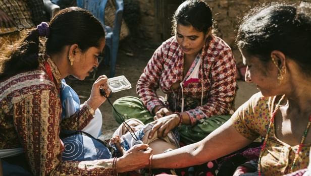 A la derecha, la voluntaria Tulsi usa un dispositivo para diagnosticar la neumonía al bebé. En el centro, su madre, Kabitea
